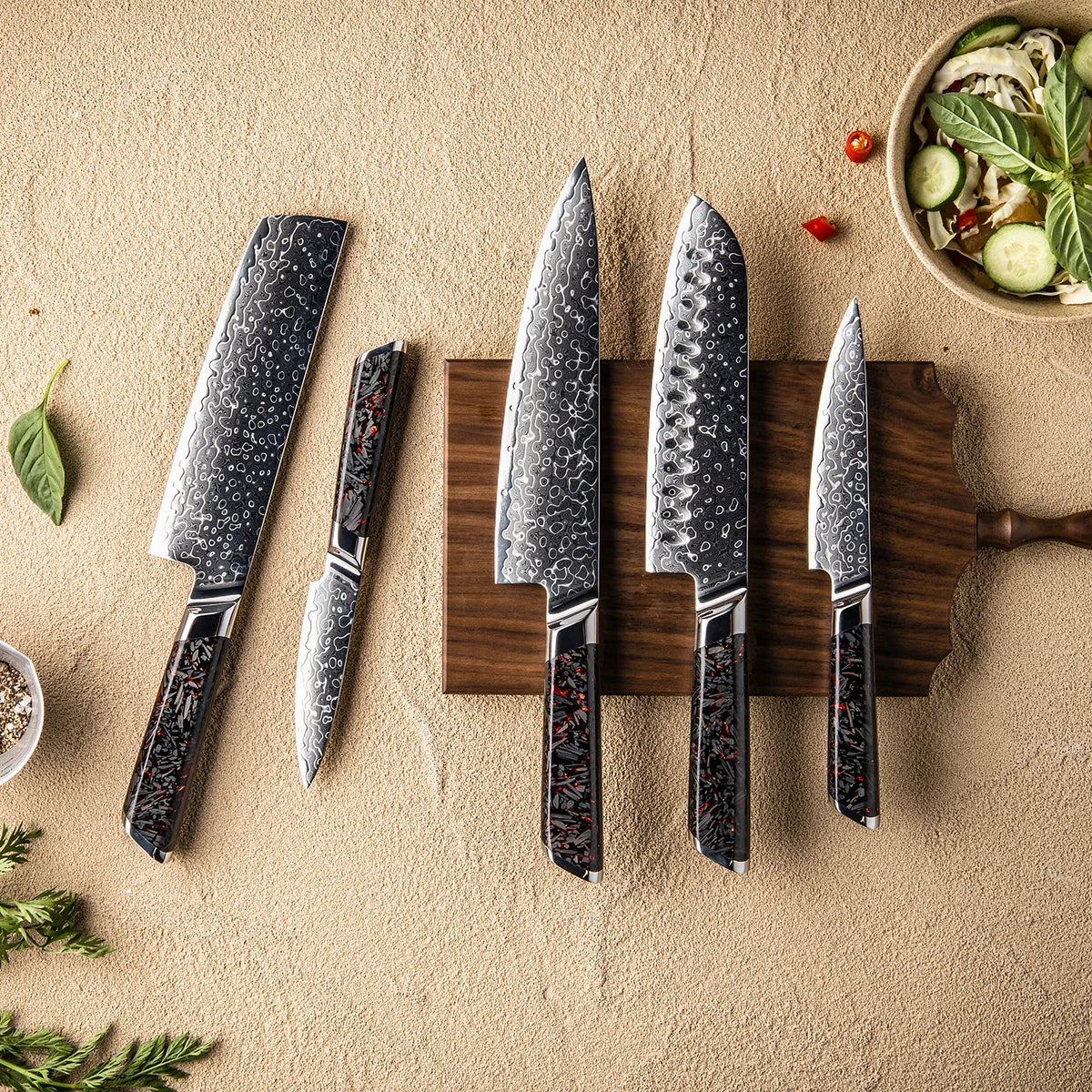 Damascus steel kitchen knives with black red handles on wood board, fresh salad nearby