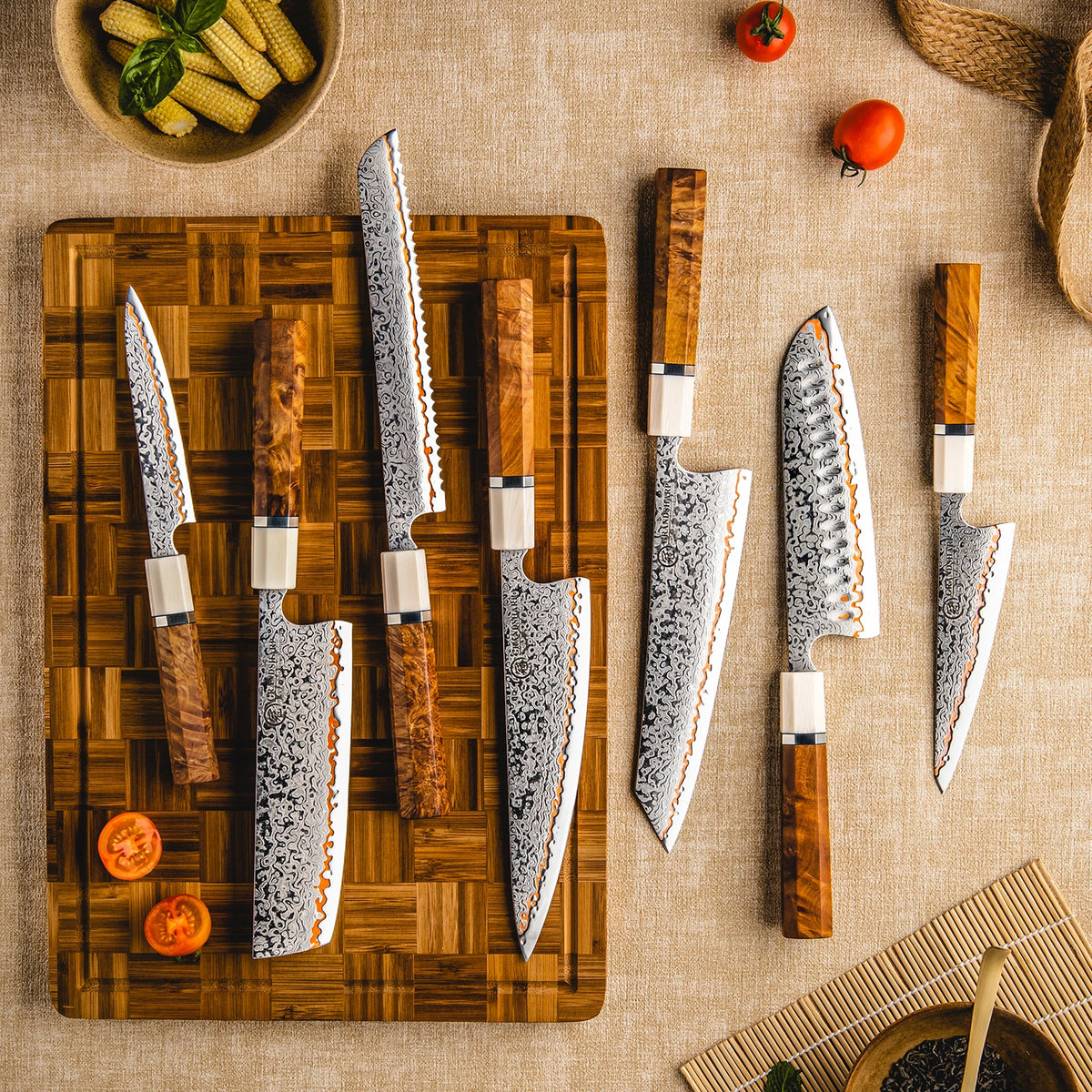 Damascus kitchen knives with wooden handles on cutting board, fresh corn and tomatoes nearby