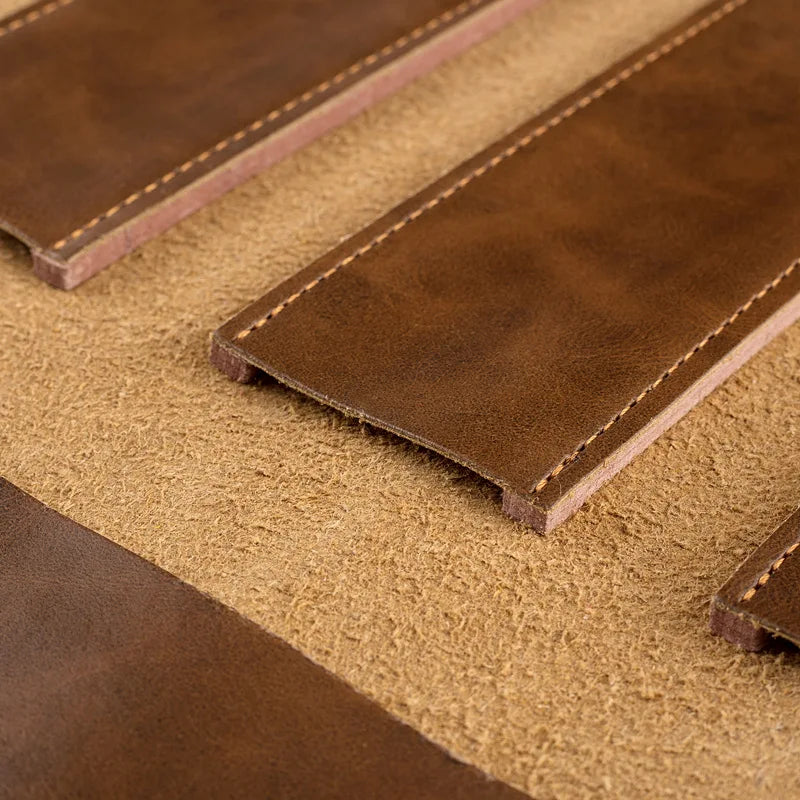 Brown leather knife sheaths with tan stitching, resting on textured fabric surface