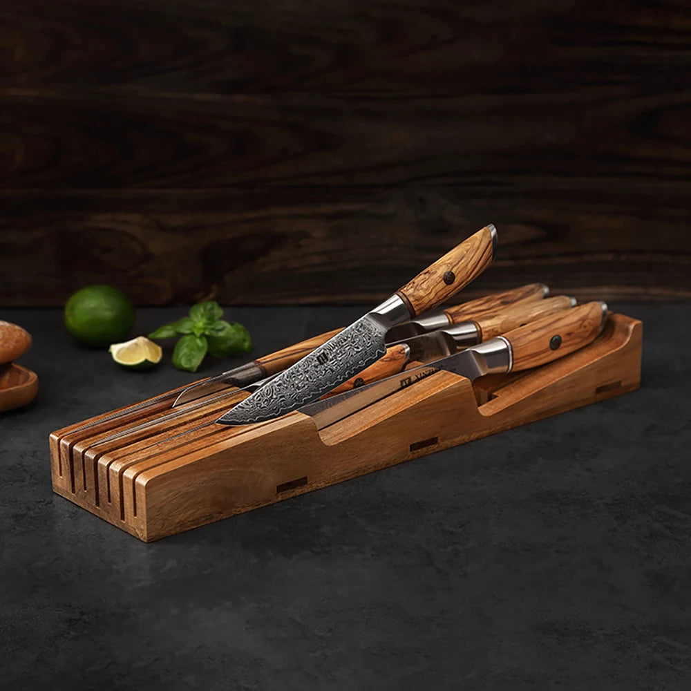 Damascus steel kitchen knives with olive wood handles in wooden block, fresh lime and basil nearby