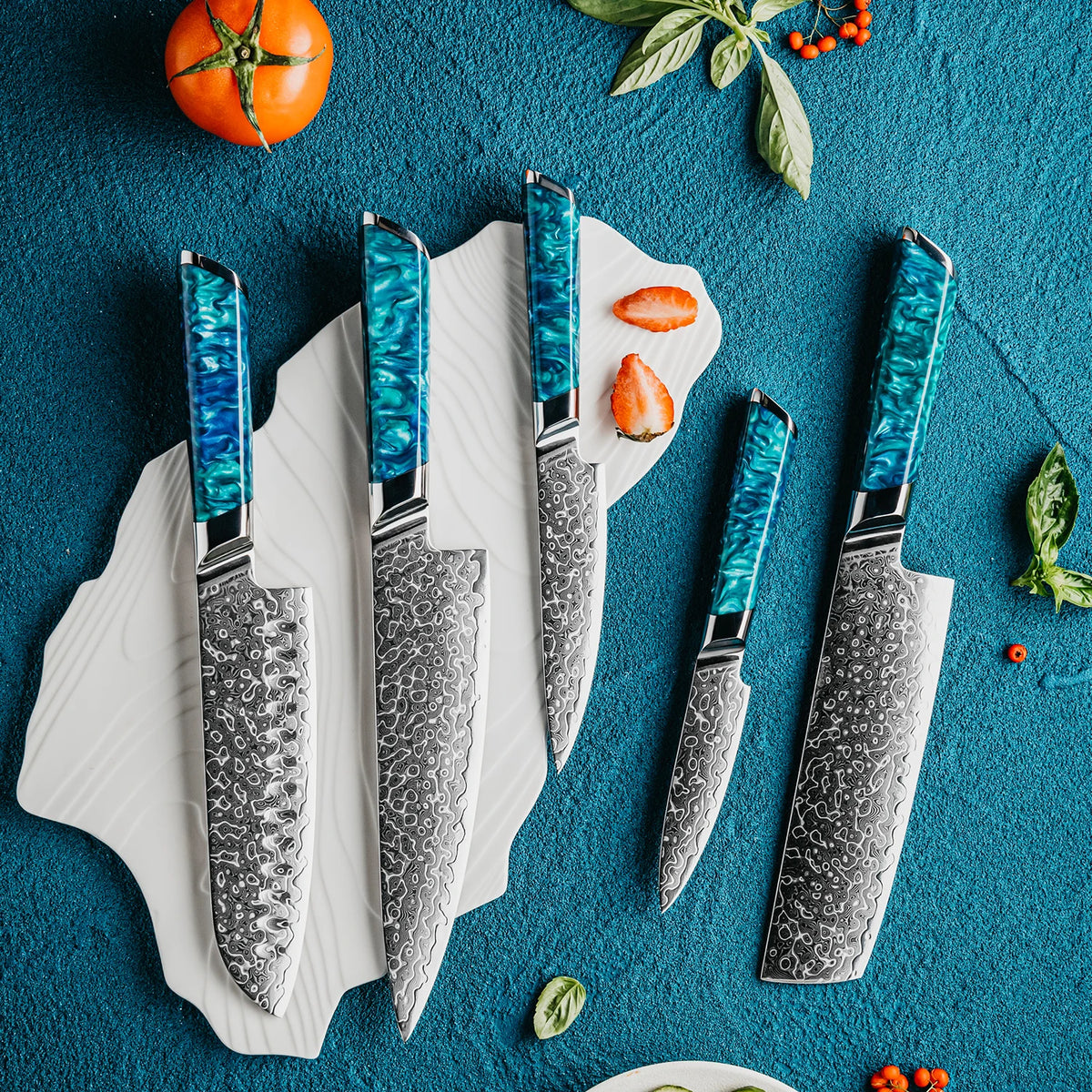 Damascus kitchen knives with blue resin handles, displayed on white plate with tomato and basil on blue background