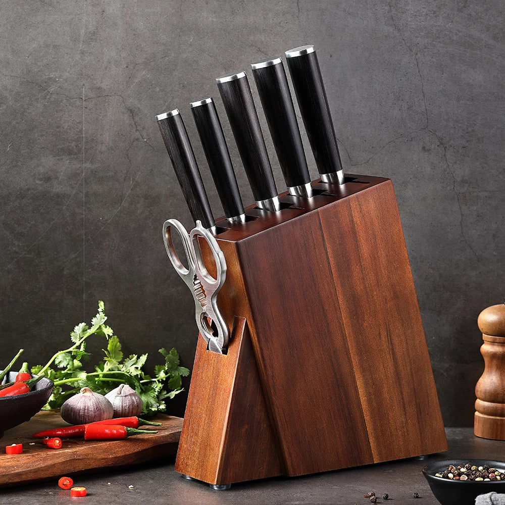Wooden knife block with black-handled kitchen knives and scissors, surrounded by fresh herbs and peppers