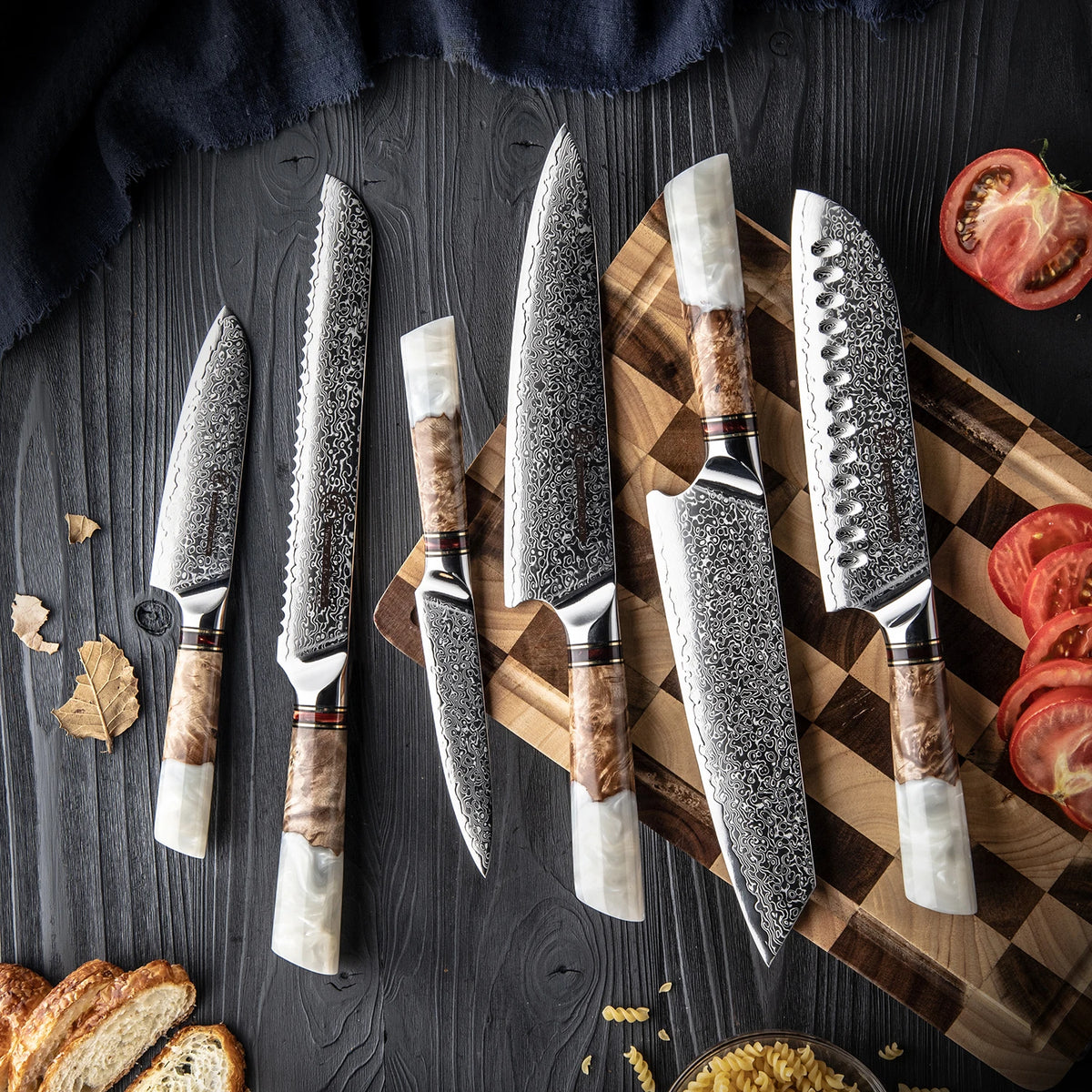 Damascus kitchen knives with wooden handles on cutting board, sliced tomato and bread nearby