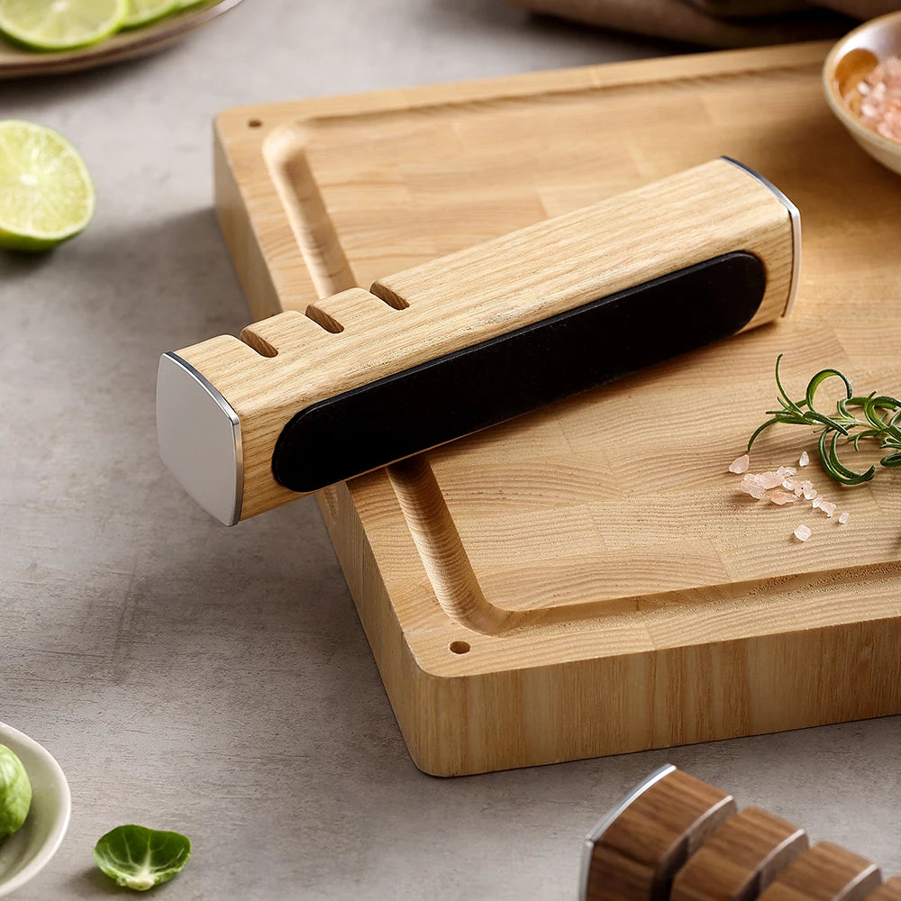 Wooden knife sharpener with black abrasive strip on cutting board, fresh herbs and lime nearby